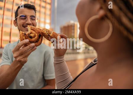 Glücklicher Mann, der süßes Essen mit einer Frau vor dem Gebäude anstoßen will Stockfoto