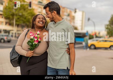 Eine glückliche junge Frau mit Blumenstrauß und einem Mann auf dem Fußweg Stockfoto