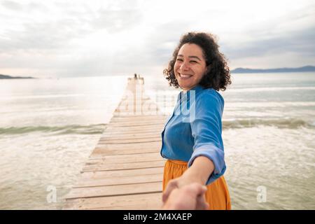 Fröhliche Frau, die Hand eines Mannes auf dem Steg inmitten des Meeres hält Stockfoto