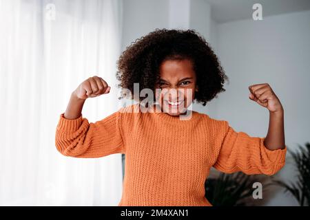 Glückliches Mädchen mit lockigen Haaren, die zu Hause Muskeln spielen Stockfoto