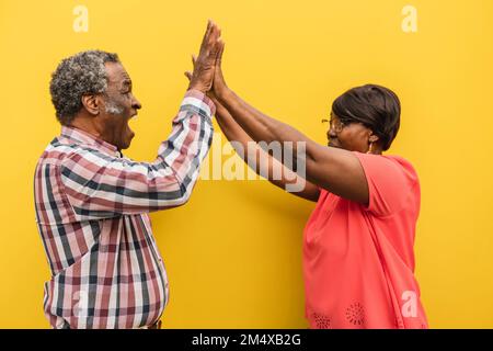 Seniorenmann und -Frau geben sich gegenseitig High-Five vor gelbem Hintergrund Stockfoto