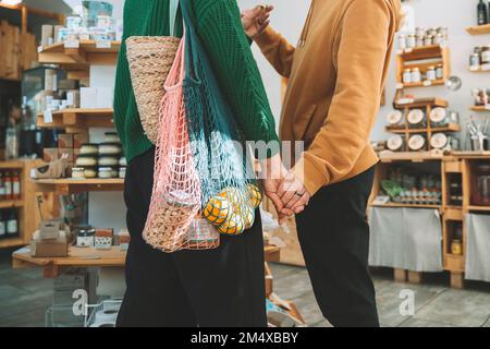 Frau mit Netztaschen, die Hand eines Mannes in einem Lebensmittelladen hält Stockfoto