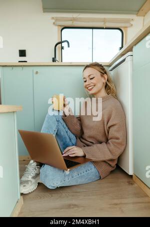 Glücklicher junger digitaler Nomade, der an einem Laptop arbeitet, der im Wohnmobil sitzt Stockfoto