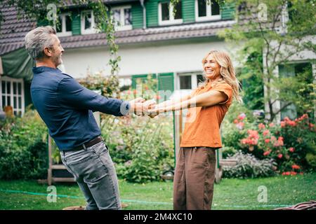 Glückliches reifes Paar, das Händchen hält und vor dem Haus Spaß hat Stockfoto