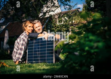 Lächelndes, reifes Paar, das an sonnigen Tagen mit Solarpaneel im Garten sitzt Stockfoto