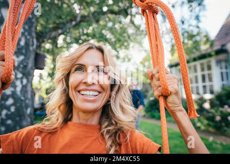 Glückliche reife Frau, die auf der Schaukel im Garten sitzt Stockfoto