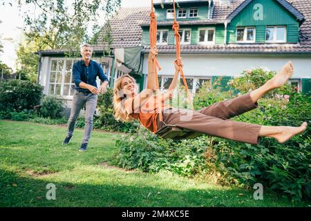 Ein glücklicher, reifer Mann mit einer Frau, die vor dem Haus die Schaukel genießt Stockfoto