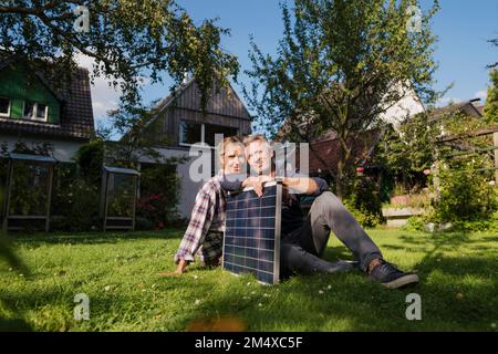 Lächelndes Paar, das mit Solarpaneel auf Gras im Garten sitzt Stockfoto