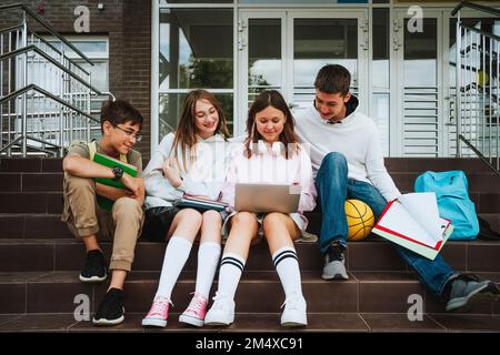 Mädchen, die Hausaufgaben über Laptop macht, von Freunden, die auf Stufen in der Schule sitzen Stockfoto