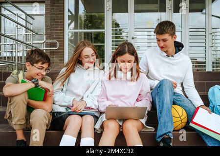 Schüler, die ihre Hausaufgaben mit einem Laptop machen, sitzen auf einer Treppe Stockfoto