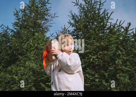 Ein Mädchen hält eine Weihnachtsgeschenkbox vor dem Tannenbaum Stockfoto