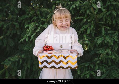 Aufgeregtes Mädchen, das eine Geschenkbox vor dem Tannenbaum hält Stockfoto