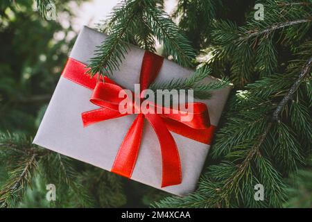Weihnachtsgeschenkbox mit rotem Band auf Tannenbaum Stockfoto