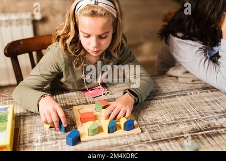 Ein Mädchen, das mit Spielzeugblöcken spielt, an einem Tisch zu Hause Stockfoto