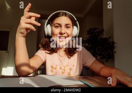 Glückliches Mädchen mit kabellosen Kopfhörern am Schreibtisch Stockfoto