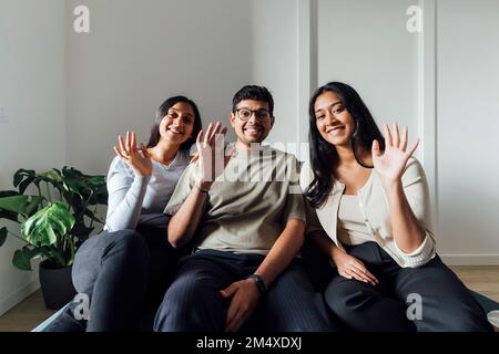 Lächelnde Frauen und Männer, die sich die Hände winken, sitzen auf dem Sofa im Wohnzimmer Stockfoto