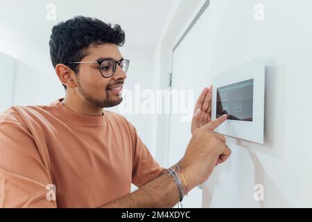 Lächelnder junger Mann mit Smart-Home-Gerät an der Wand Stockfoto