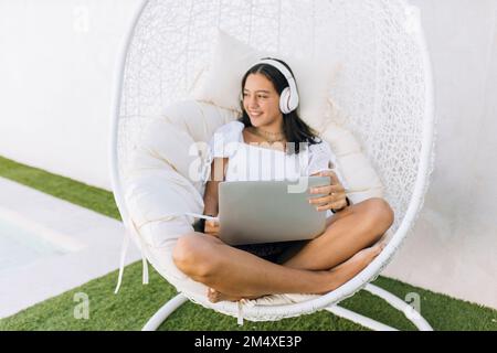 Ein aufmerksames Mädchen, das mit einem Laptop auf einem Hängestuhl sitzt Stockfoto