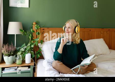 Eine denkwürdige Frau, die im Schlafzimmer Kopfhörer mit Notebook trägt Stockfoto