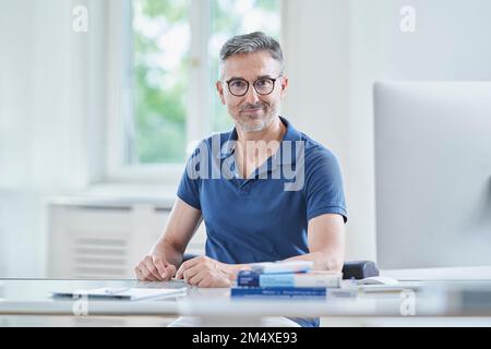 Selbstbewusster Arzt trägt eine Brille, sitzt am Schreibtisch in der ärztlichen Praxis Stockfoto