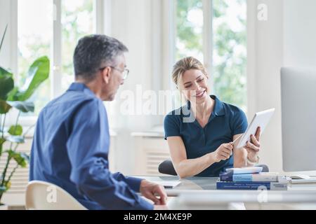 Lächelnde Arztin, die mit der Patientin über Tablet PC in der Praxis spricht Stockfoto