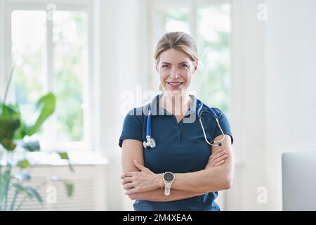 Glückliche Arztin im Stehen mit Stethoskop in der ärztlichen Praxis Stockfoto