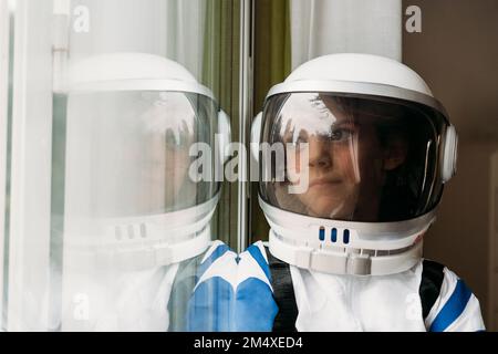 Eine rücksichtsvolle Frau in einem Raumkostüm, die zu Hause durch das Fenster schaut Stockfoto