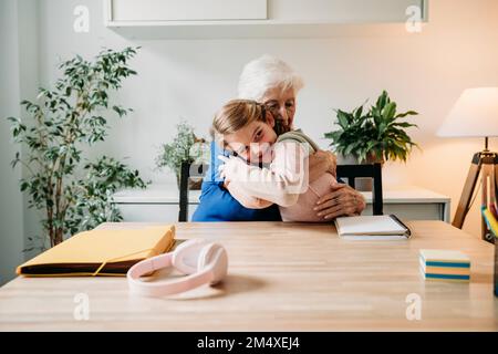 Glückliches Mädchen, das Großmutter zu Hause umarmt Stockfoto