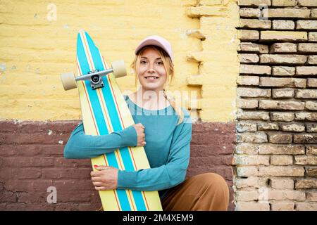 Lächelnde Frau mit Mütze und Skateboard vor der Wand Stockfoto