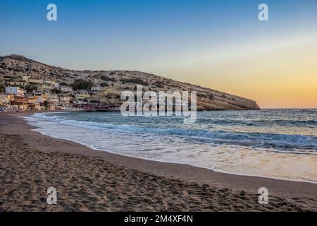 Griechenland, Kreta, Matala, Matala Beach in der Abenddämmerung mit Dorf im Hintergrund Stockfoto