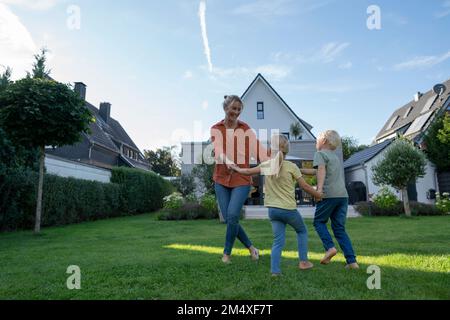 Verspielte Mutter, die mit Kindern im Garten um Rosy herumspielt Stockfoto