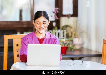 Lächelndes medizinisches Fachpersonal, das zu Hause ein Notebook benutzt Stockfoto