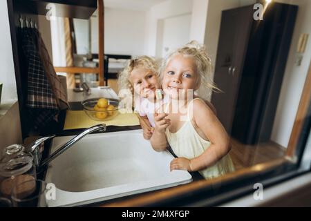 Lächelnde Mädchen, die Zahnbürsten aus Holz in der Küche zeigen Stockfoto