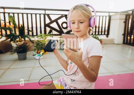 Frau mit Kopfhörern, die auf der Terrasse ein Mobiltelefon benutzt Stockfoto