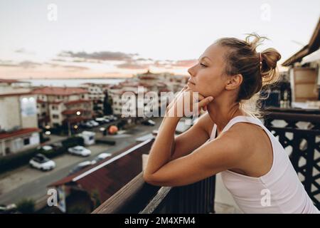 Frau lehnte sich beim Sonnenuntergang auf die Dachterrasse und schaute auf die Aussicht Stockfoto