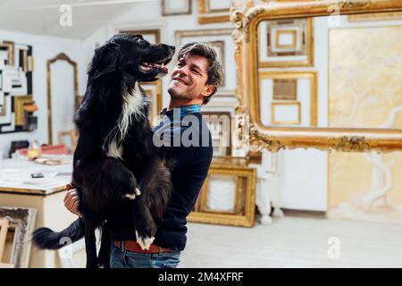 Lächelnder reifer Mann mit Hund in der Werkstatt Stockfoto