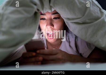 Ich habe eine junge Frau überrascht, die zu Hause ein Smartphone im Bett benutzt hat Stockfoto