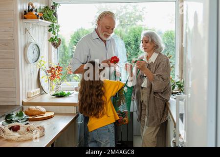 Großeltern und Enkelin packen frische Lebensmittel in der Küche aus Stockfoto