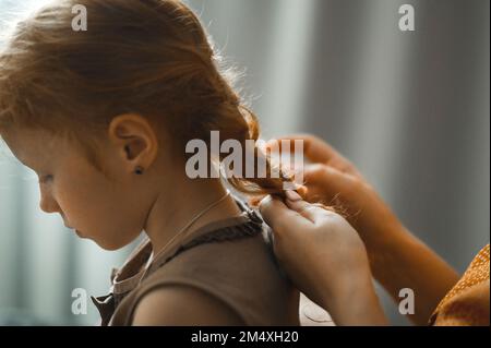 Mutter, die die Haare ihrer Tochter zu Hause geflochten hat Stockfoto