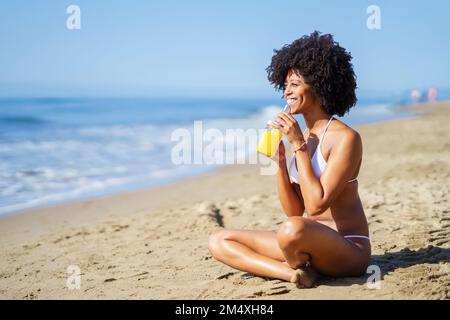 Glückliche Frau, die im Sommer Orangensaft am Strand trinkt Stockfoto