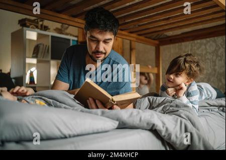 Vater liest seinen Söhnen zu Hause im Bett ein Buch vor Stockfoto