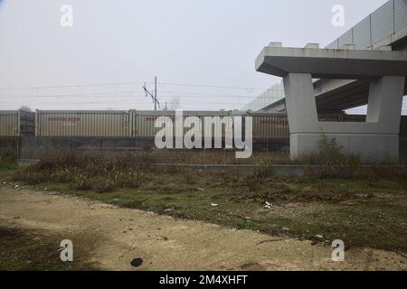 Eisenbahnstrecke mit Güterwagen, die an einem nebligen Tag unter einem Viadukt vorbeifahren Stockfoto