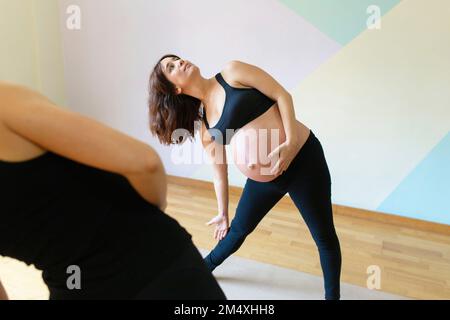 Schwangere Frau, die sich mit einer Lehrerin im Yoga-Studio streckt Stockfoto
