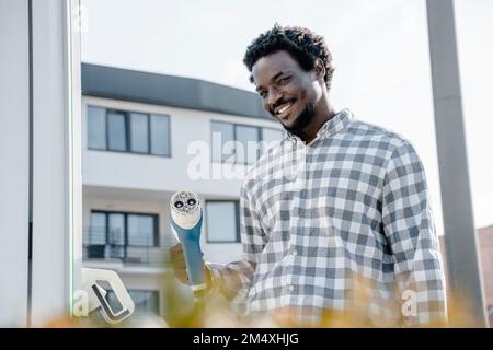 Junger Mann mit Elektroauto-Ladegerät an der Station Stockfoto