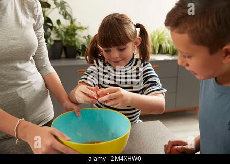 Lächelndes Mädchen, das Schwester hilft, Kekse von Bruder zuhause zuzubereiten Stockfoto