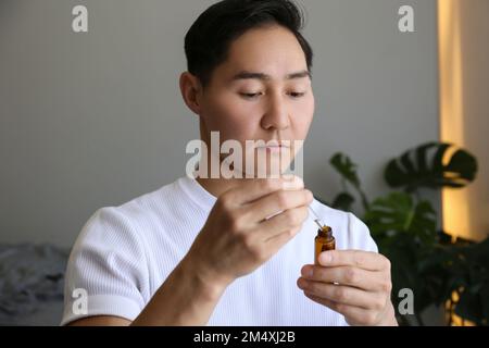 Junger Mann, der zu Hause Serum in der Hand hat Stockfoto