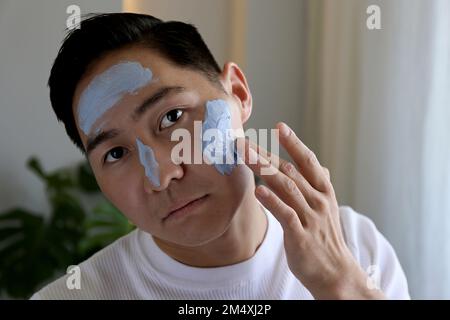 Junger Mann, der zu Hause eine Maske aufträgt Stockfoto