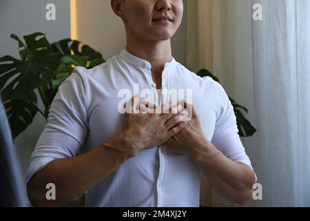 Lächelnder Mann mit Händen auf der Brust zu Hause Stockfoto