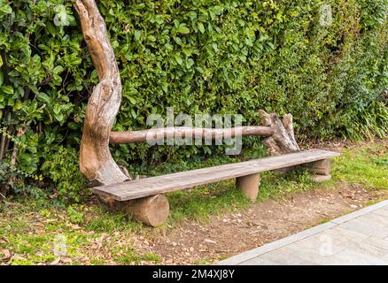 Handgefertigte Holzbänke im Park, umgeben von grünen Büschen. Stockfoto