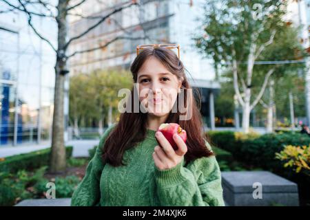 Lächelnde Frau, die einen Apfel vor dem Gebäude hält Stockfoto